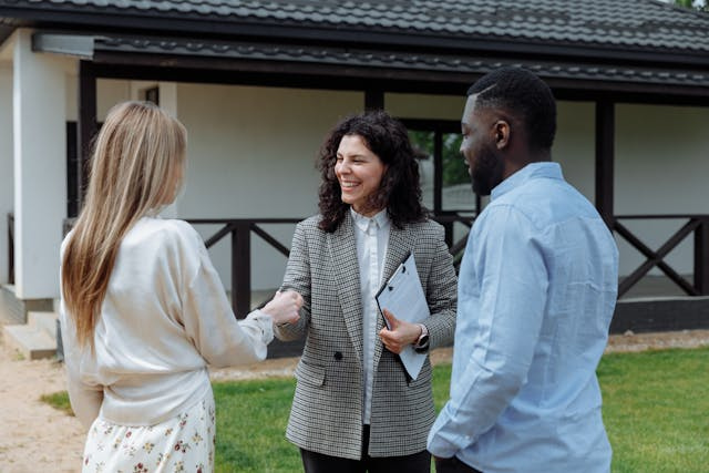 two people shaking hands with a property manager in front of a house